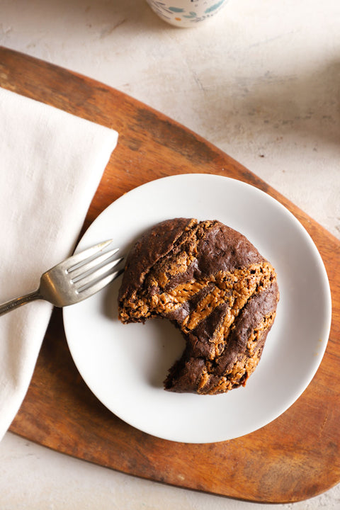 Chocolate chia cookie with a bite taken out on a white plate with a fork on a wooden board.