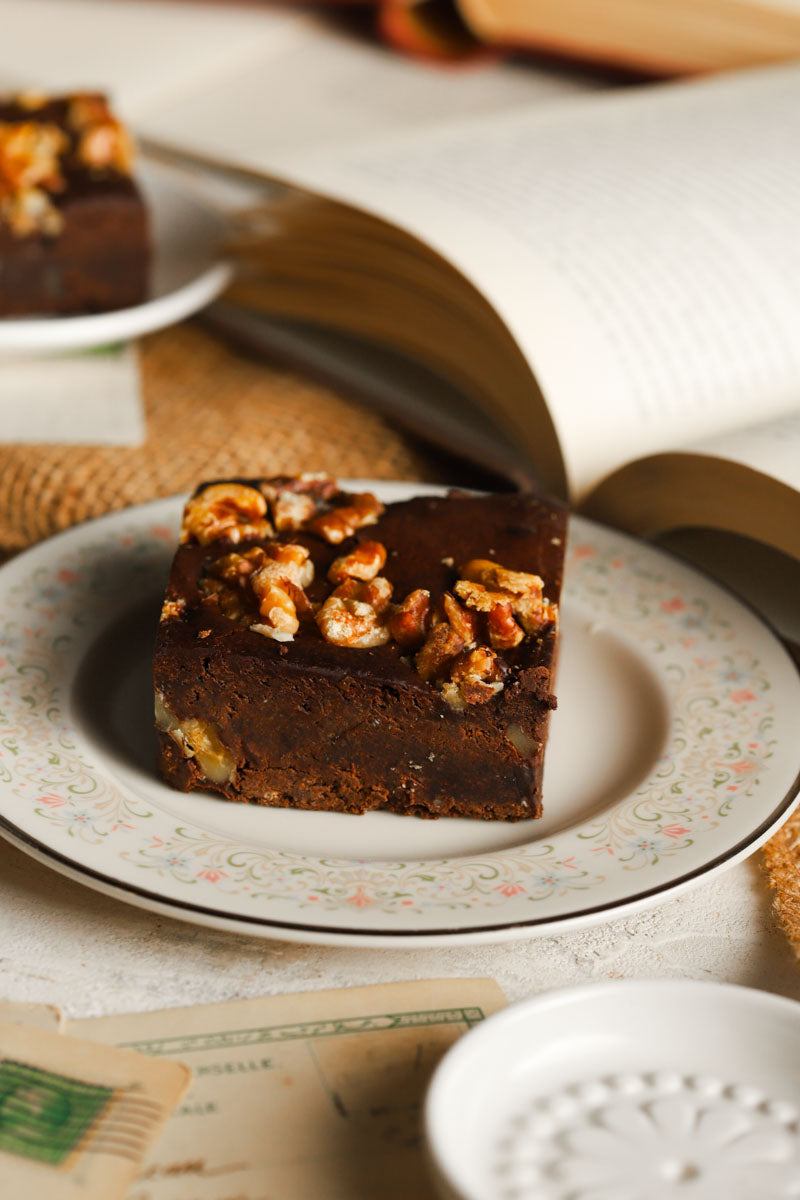 Walnut brownie on a decorative plate with a book in the background
