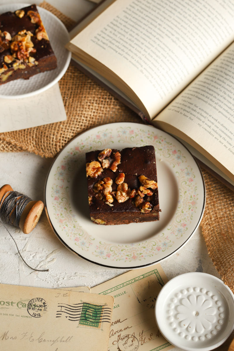 Walnut brownies on decorative plates next to a book and vintage postcards