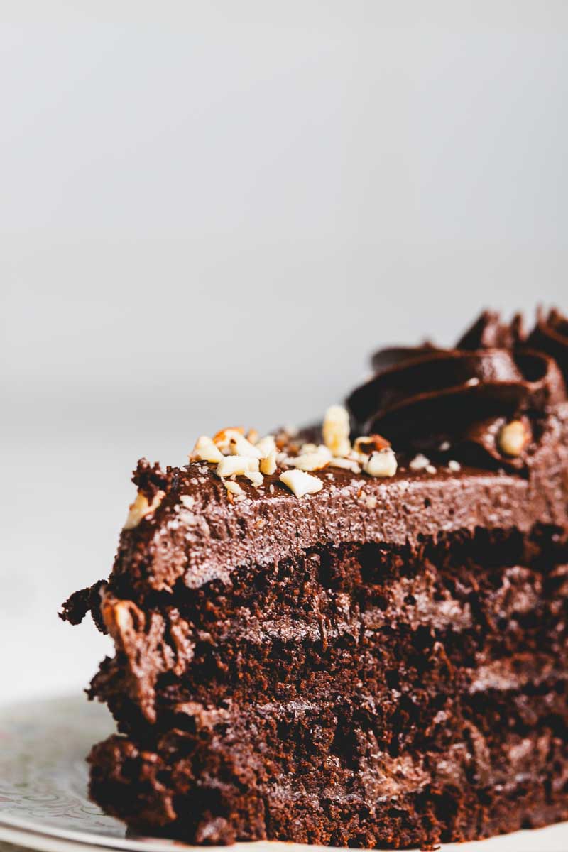 close up of a slice of keto chocolate cake with rich chocolate frosting and chocolate crumble and nut decoration