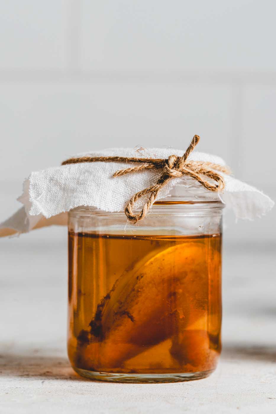 small glass jar of komucha with a scoby floating inside. a cloth is tied over the top.
