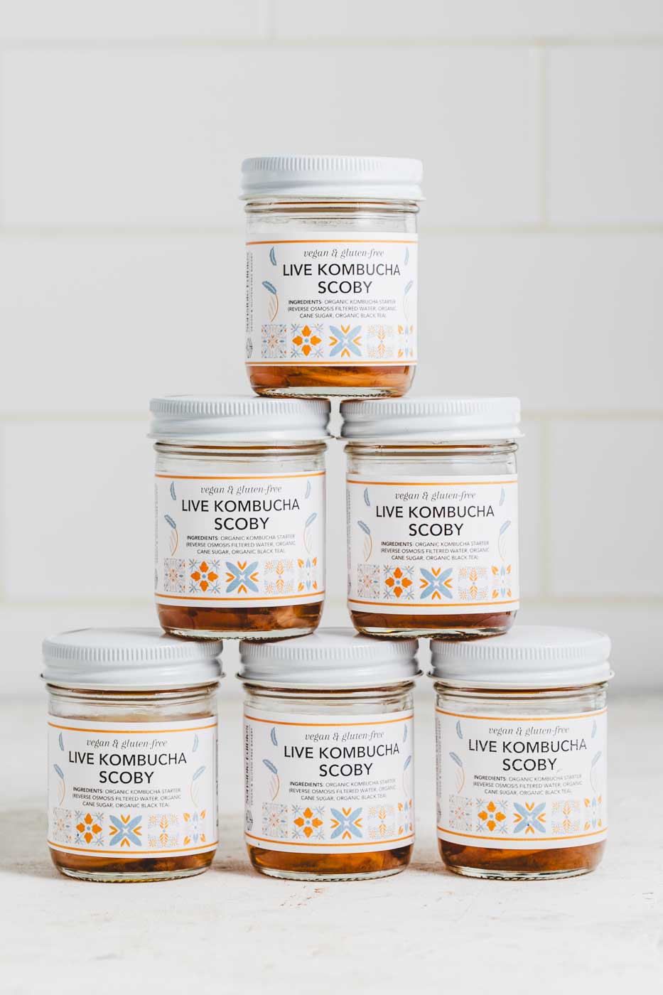 Six jars of live kombucha scobies stacked in a pyramid on a white background