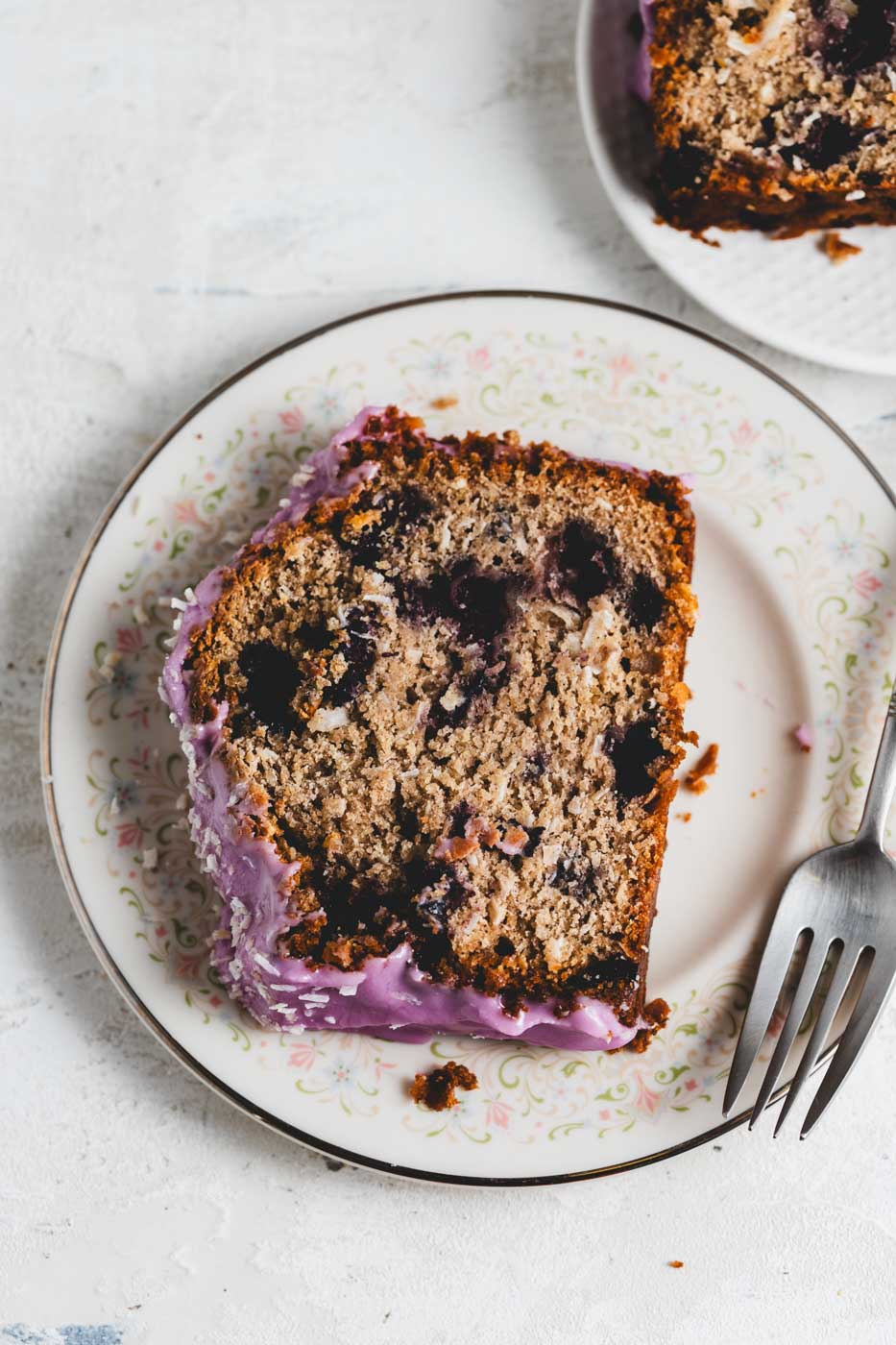 close up of slices of a coconut loaf with blueberries throughout and a vibrant purple blueberry icing garnished with shredded coconut