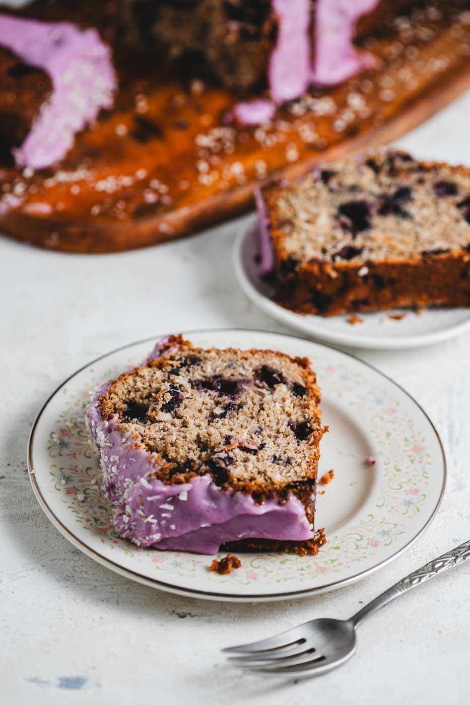 close up of slices of a coconut loaf with blueberries throughout and a vibrant purple blueberry icing garnished with shredded coconut