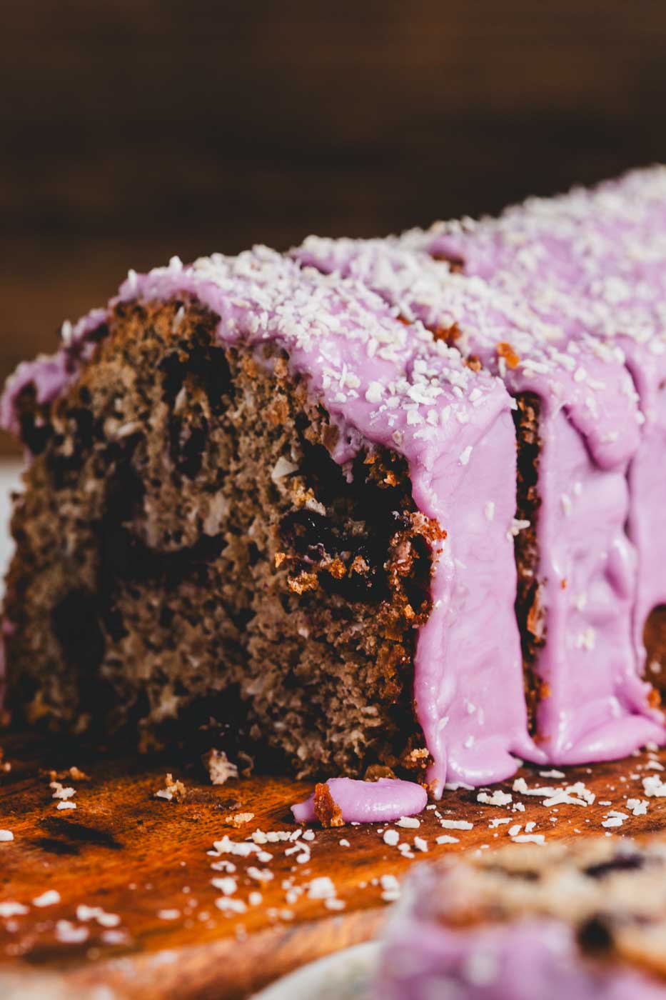 close up of a sliced coconut loaf with blueberries throughout and a vibrant purple blueberry icing garnished with shredded coconut