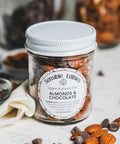 A jar of Sensible Edibles Almonds & Chocolate. The jar contains whole almonds and chocolate chunks, and is surrounded by scattered almonds and chocolate pieces.