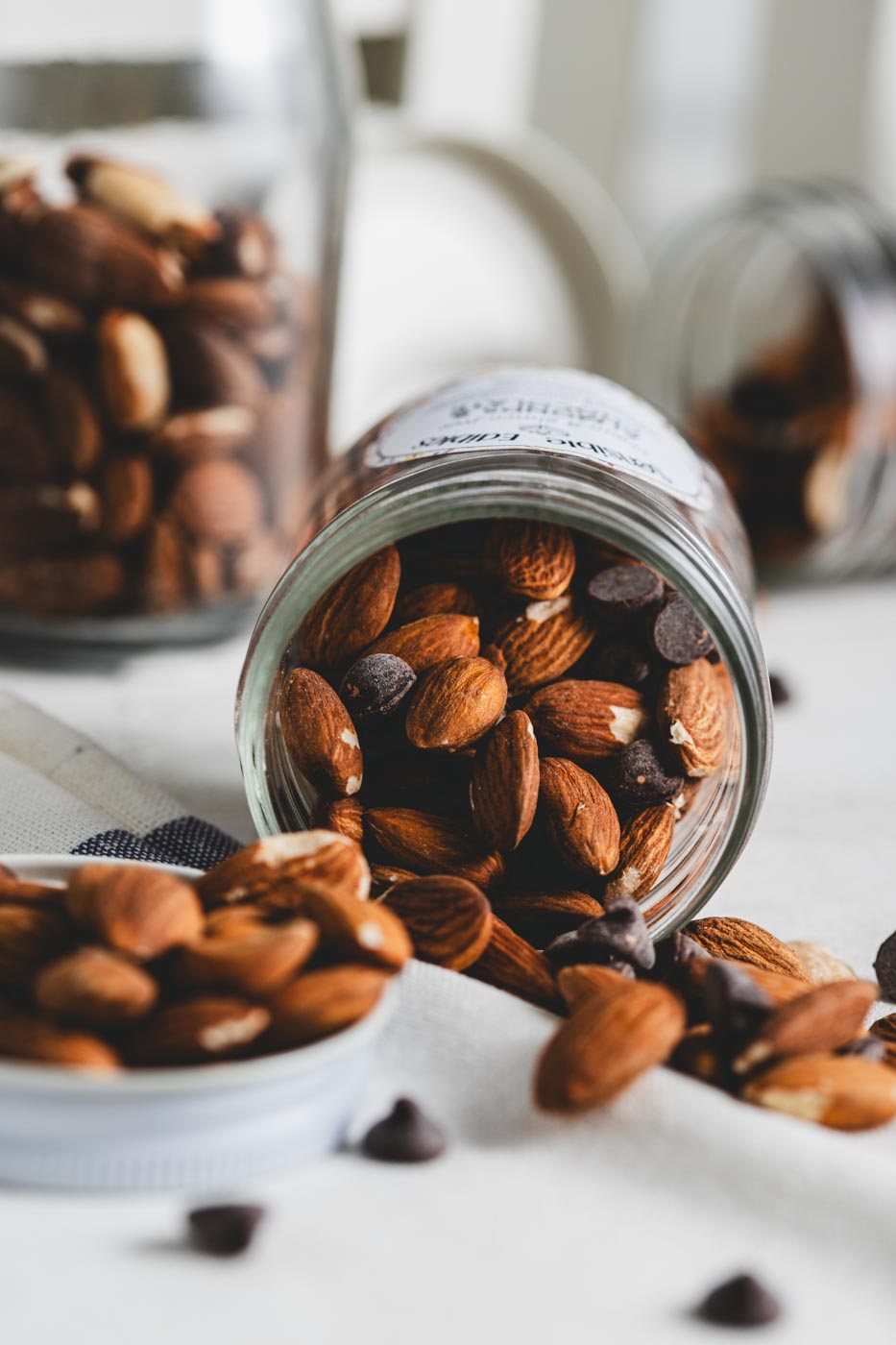 A jar of Sensible Edibles Almonds & Chocolate tipped over, spilling whole almonds and chocolate chunks onto a white cloth.