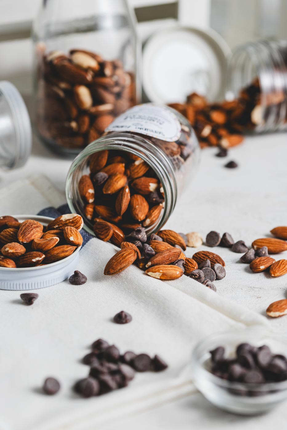 A jar of Sensible Edibles Almonds & Chocolate tipped over, spilling whole almonds and chocolate chunks onto a white cloth.