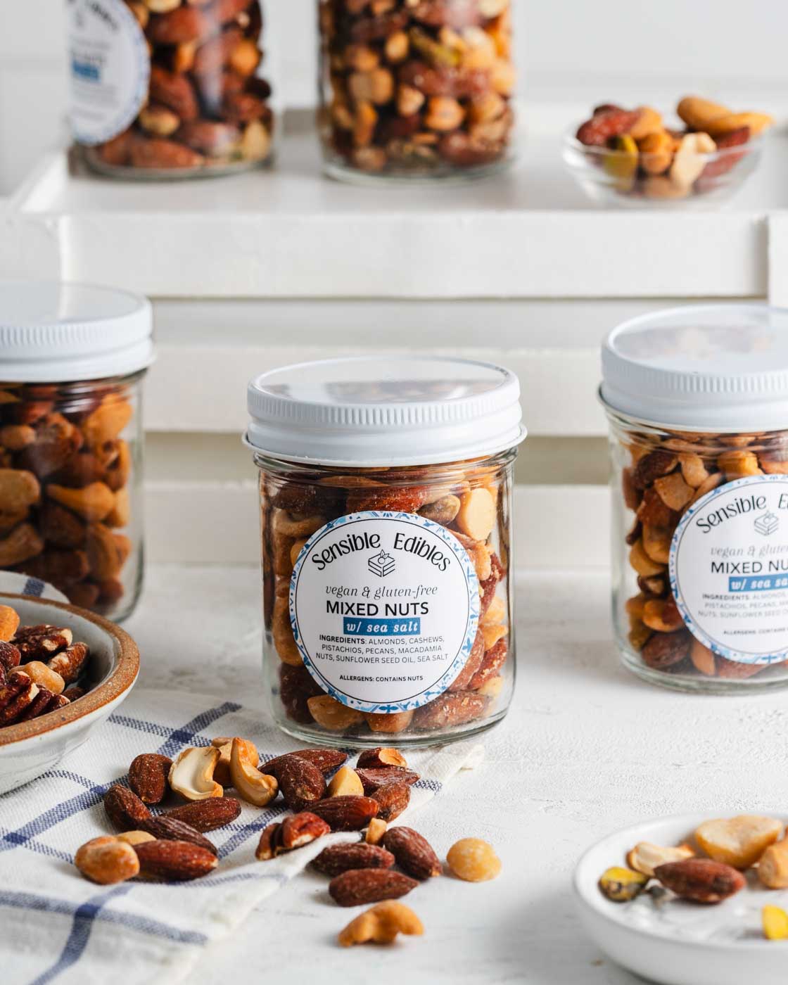 Jars of salted mixed nuts with more nuts piled around them