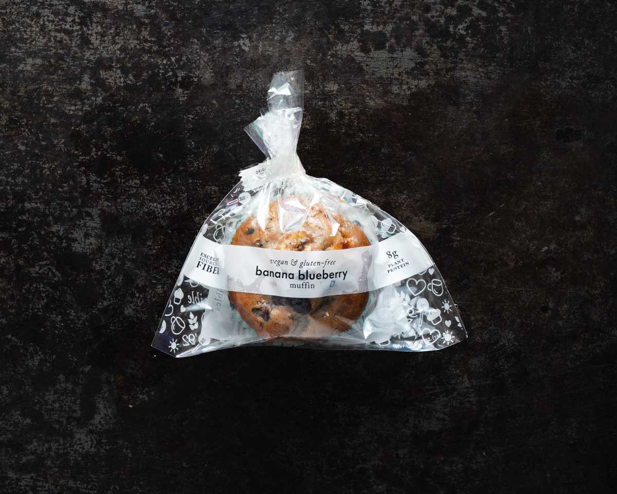 Packaged banana blueberry muffin on a textured black background.