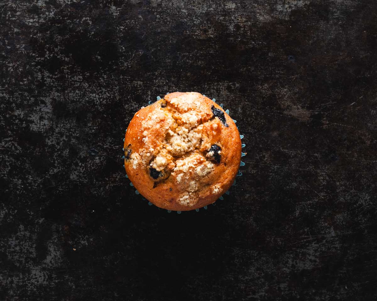 Top view of a blueberry crumb muffin on a dark textured background.