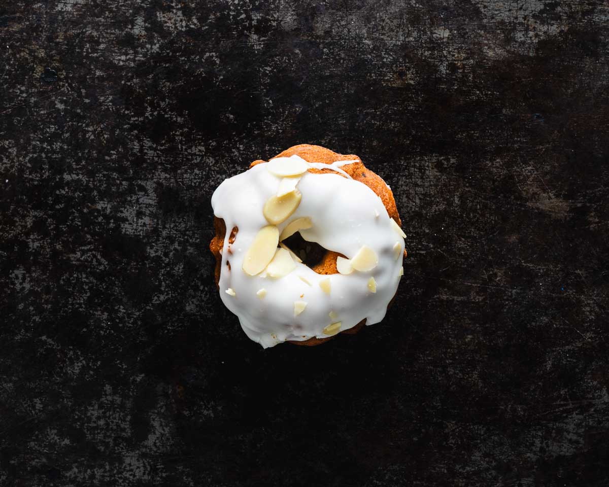 Top view of a mini lemon almond bundt cake with white icing and almond slices on a dark background.