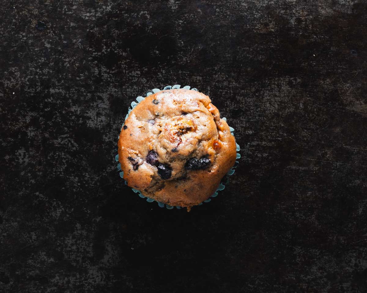 Top view of a banana blueberry muffin on a textured black background.