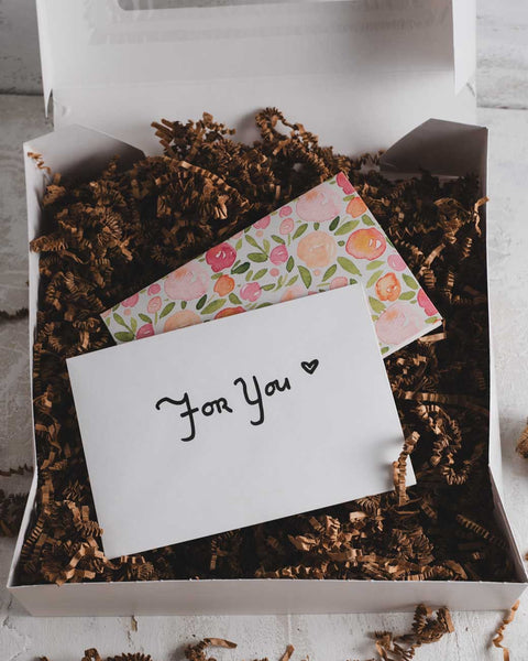 Valentine's gift box with a floral card and an envelope labeled 'For You' on top of brown shredded paper.