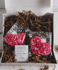 Valentine's gift box containing two heart-shaped cookies with pink frosting, with a label for 'Sensible Edibles Sweet Heart Cookies' on top of brown shredded paper.