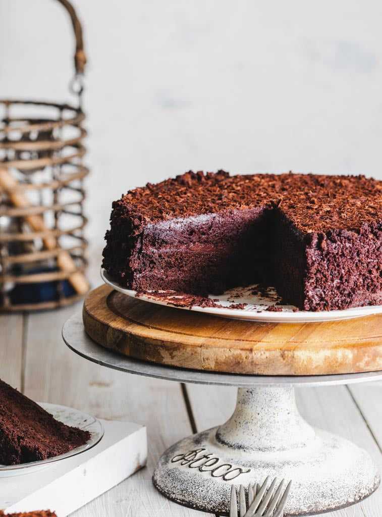 Chocolate fudge cake with a slice missing, showcasing its rich, layered interior, displayed on a cake stand.