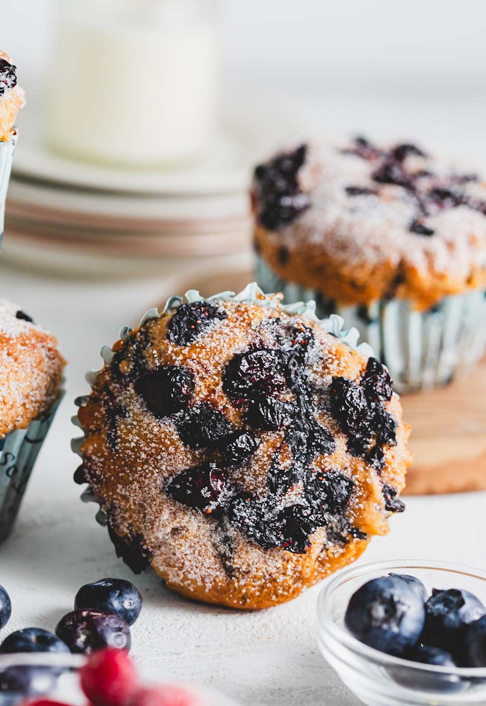 Vanilla berry muffin with mixed berries and powdered sugar on top, placed upright with more muffins and berries in the background.