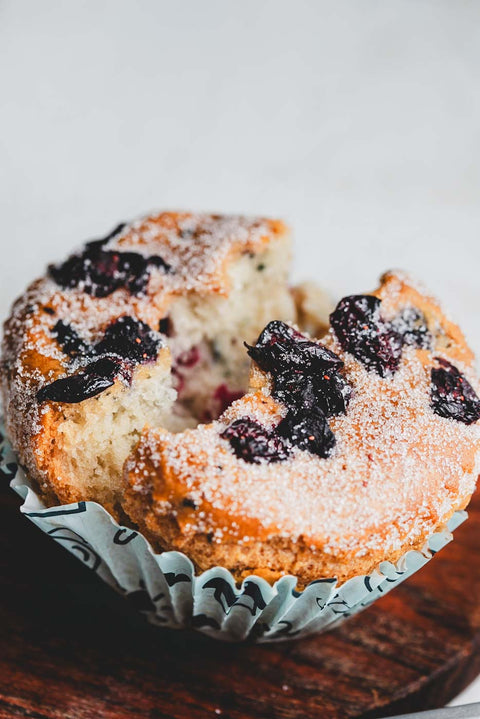 Vanilla berry muffin split in half, showing a soft, fluffy interior with visible berries, sprinkled with powdered sugar.