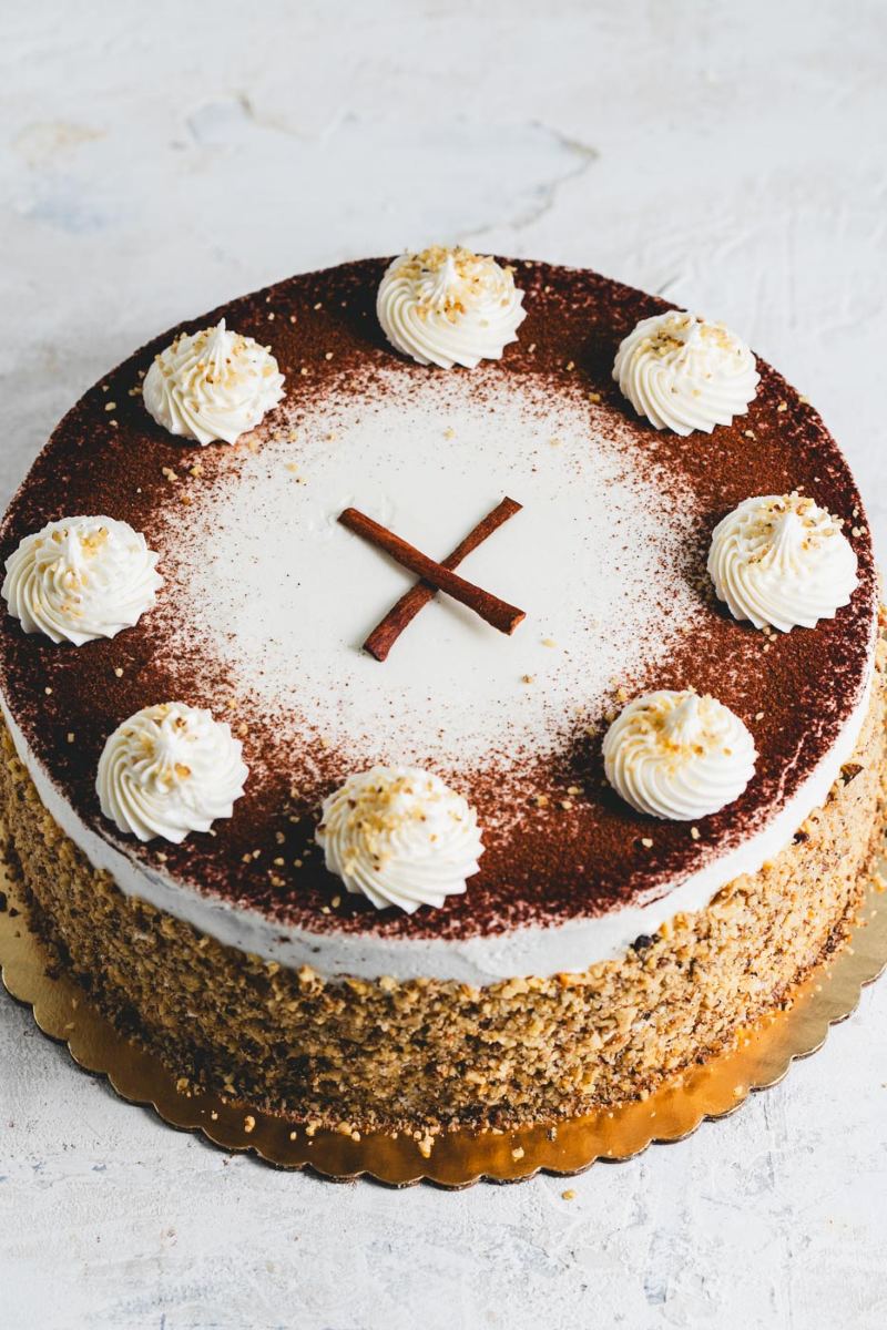 A cake with white frosting dusted with cooca powder and rolled in crushed nuts with white icing and cinnamon stick decoration