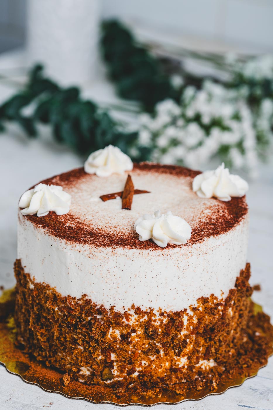 A carrot cake with white frosting dusted with cooca powder and rolled in cake crumbs with white icing and cinnamon stick decoration