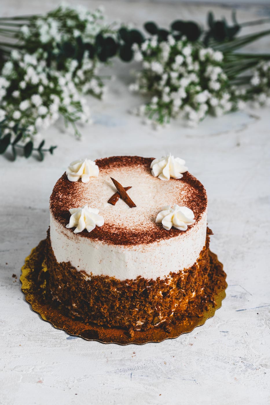 A carrot cake with white frosting dusted with cooca powder and rolled in cake crumbs with white icing and cinnamon stick decoration