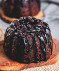 A chocolate bundt cake with chocolate glaze on top, served on a wooden plate.