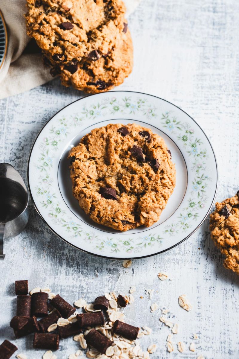 An oatmeal chocolate chunk cookie on a white plate with chocolate chunks and oats spread around it