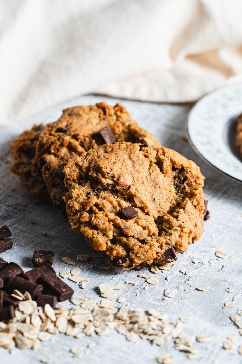 Oatmeal chocolate chip cookies stacked on a light background with chocolate pieces and oats scattered around