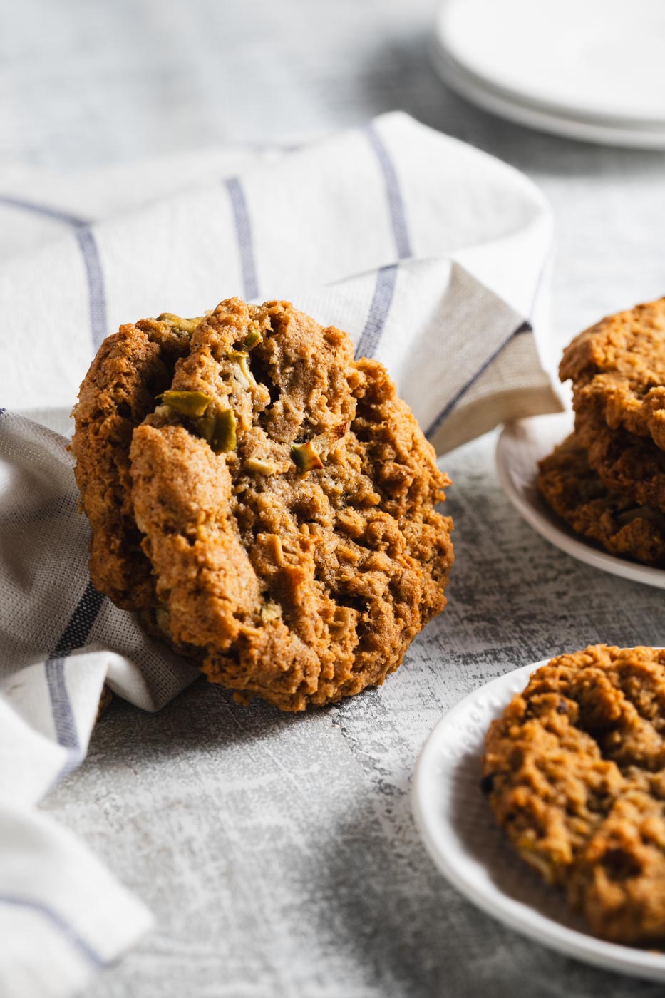 Apple oatmeal cookies stacked on white plates and leaning against a white cloth