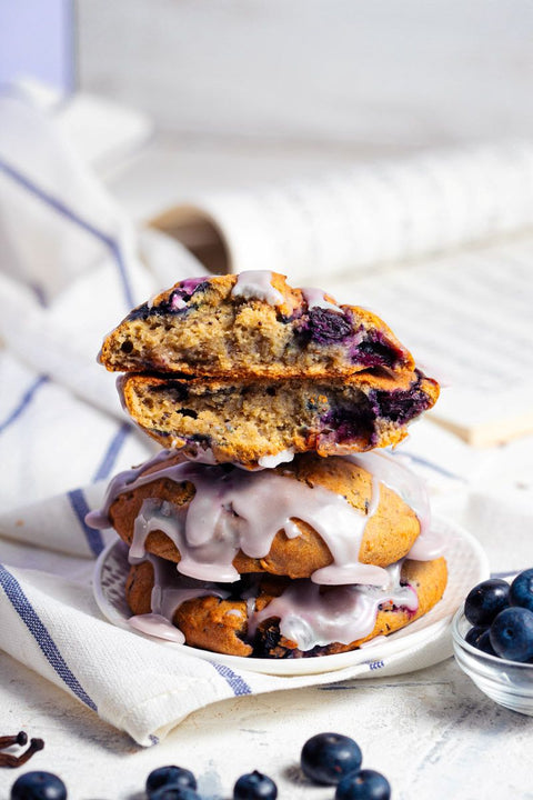 Stack of blueberry lemon scones with a lemon glaze on a white plate, surrounded by blueberries.