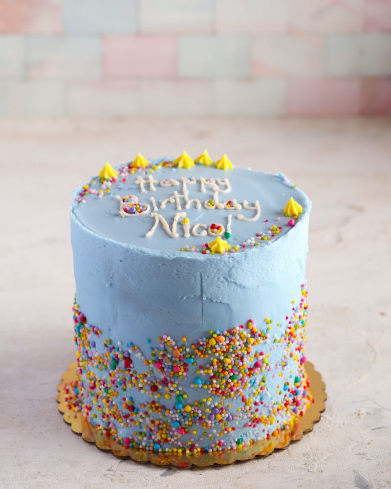 Blue birthday cake with colorful sprinkles, yellow icing accents, and 'Happy Birthday Nico' text 