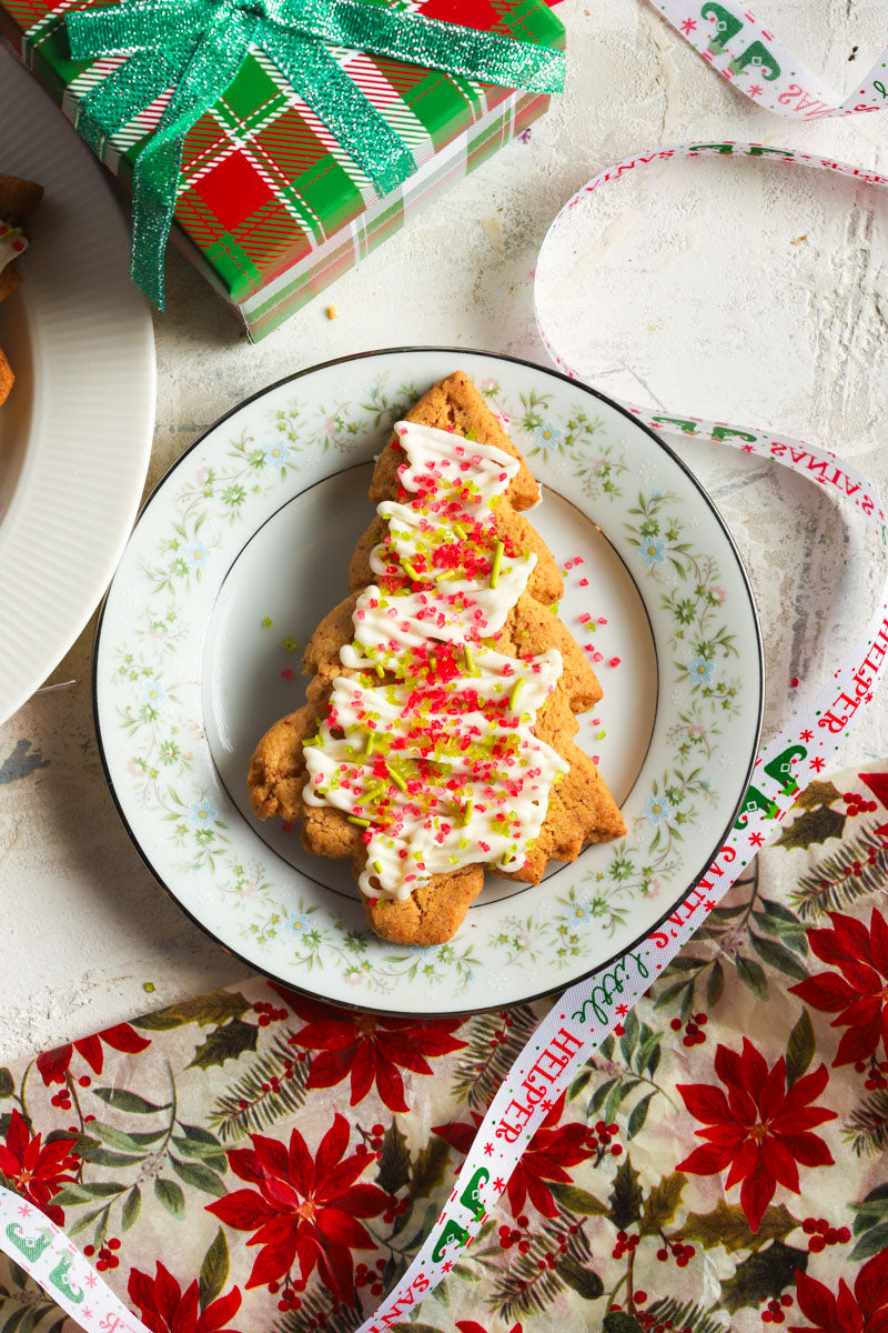 Frosted christmas cookie with red and green sprinkles on a plate with decorative paper and gift box in the background