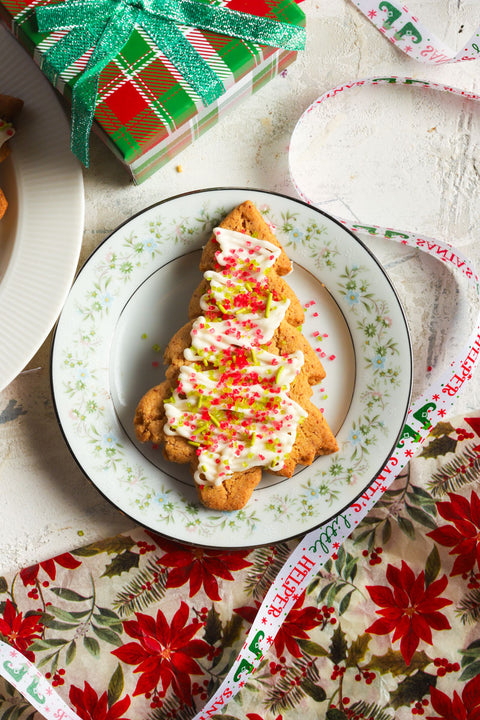 Frosted christmas cookie with red and green sprinkles on a plate with decorative paper and gift box in the background