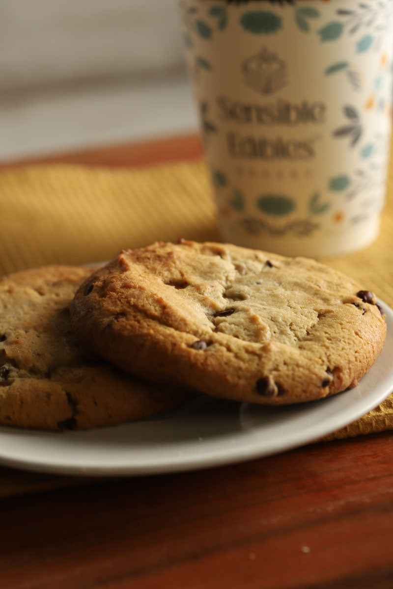 Two cookies on a plate with a coffee cup labeled 'Sensible Fabrics' in the background.