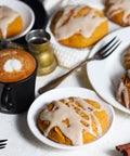 Pumpkin scones with cheesecake icing on white and black plates with cinnamon and coffee