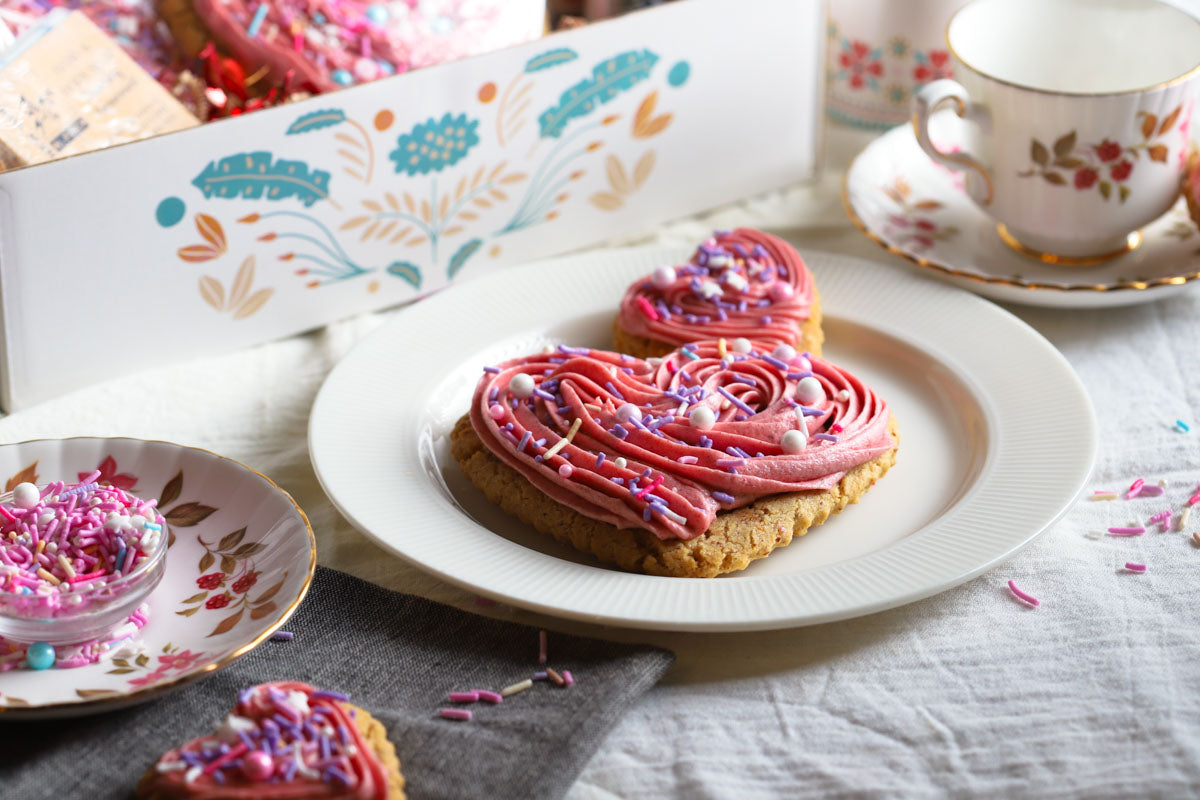 Heart-shaped cookies with pink frosting on a white plate, surrounded by decorative items.
