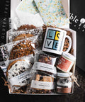 Warmth & Wellness gift box with assorted cookies, a 'LOVE' mug, oatmeal brookie, raspberry hazelnut bar, chocolate jar, vegan candle, and a floral card.