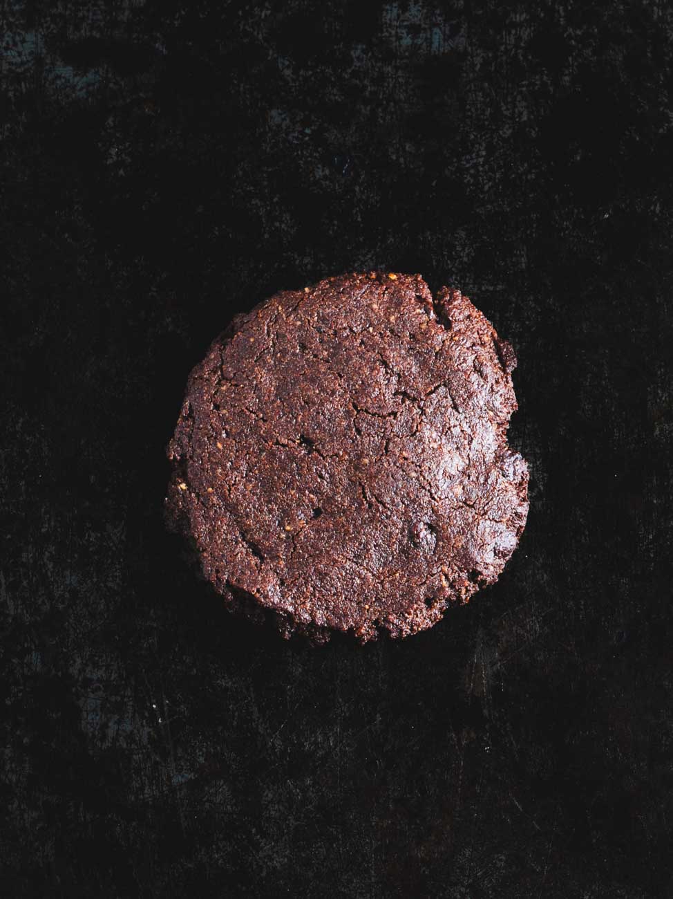 Milk chocolate cookie on a dark background, highlighting its rich texture and crumbled edges.