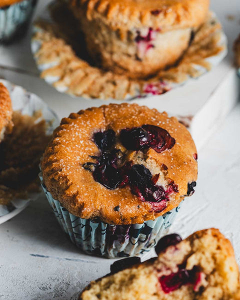 Close-up of a cinnamon pumpkin muffin with cranberries, highlighting the moist texture and cranberries on top, with more muffins in the background.