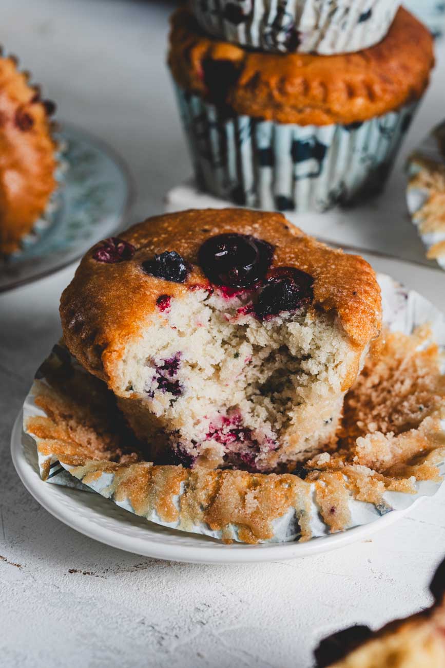 A bitten cinnamon pumpkin muffin with cranberries, placed on a white plate, showing the moist and fluffy interior with cranberries.
