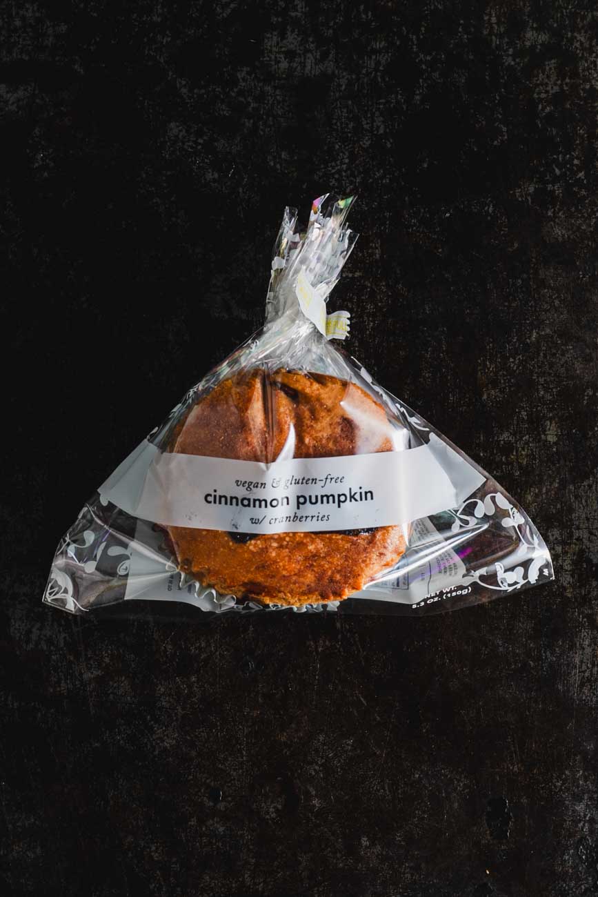 Packaged cinnamon pumpkin muffin with cranberries from Sensible Edibles Bakery, labeled as vegan and gluten-free, on a dark background.