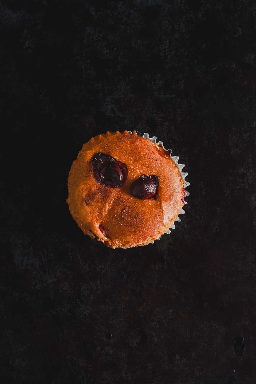 Top view of a single cinnamon pumpkin muffin with cranberries, showcasing the golden-brown top with visible cranberries, on a dark background.