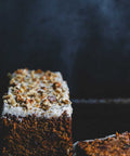 Carrot walnut loaf topped with creamy frosting and crushed walnuts displayed on a decorative plate.
