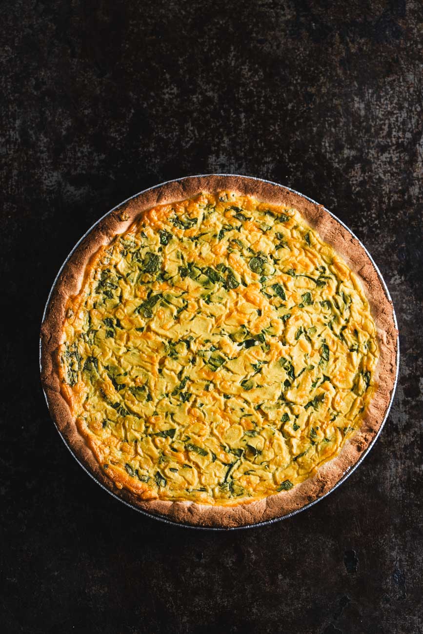 Whole spinach cheddar quiche on a dark background.