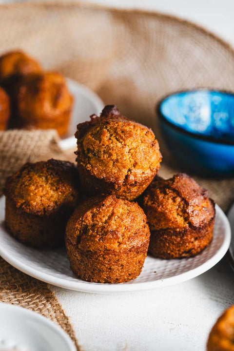 A close-up of a white plate filled with a pile of golden-brown muffins, set against a burlap background.