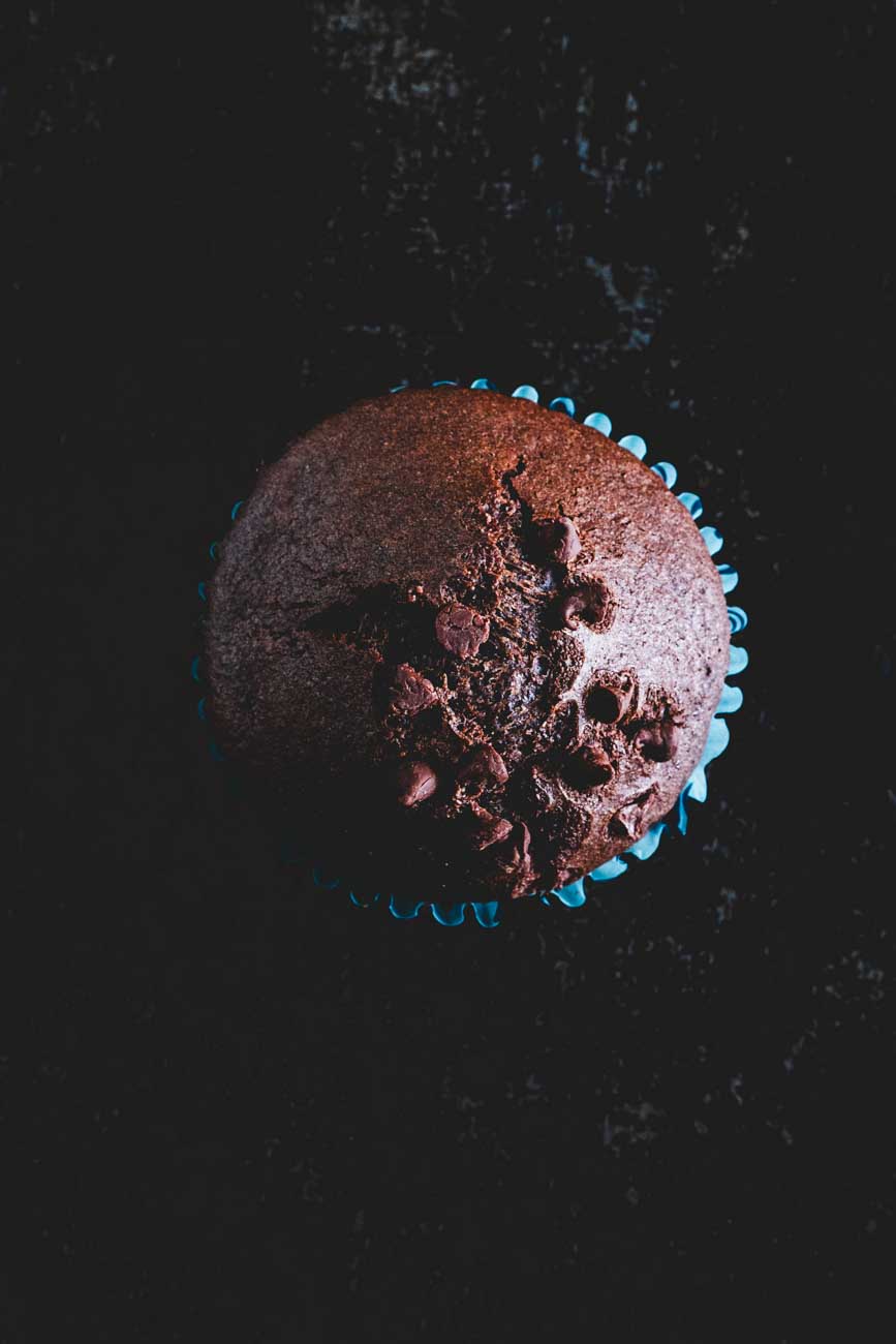 Top view of a cocoa bean muffin with chocolate chips on a dark background, highlighting its moist texture.