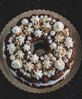 Large carrot walnut bundt cake with creamy frosting and crushed walnuts on a scalloped-edge cake board, featuring intricate frosting designs
