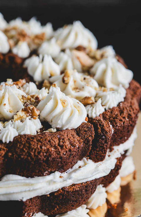 Close-up of a carrot walnut bundt cake with intricate frosting design and crushed walnuts.