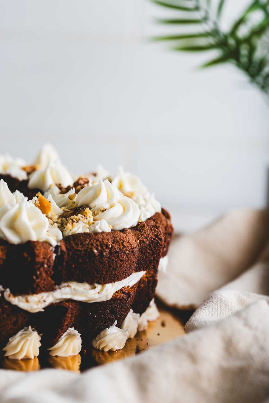 A carrot walnut bundt cake with intricate creamy frosting and crushed walnuts.