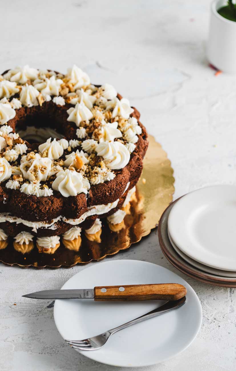 A carrot walnut bundt cake with intricate creamy frosting and crushed walnuts.